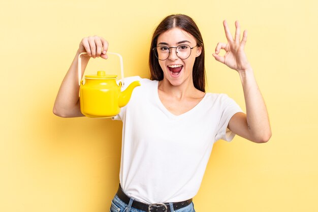 Young hispanic woman feeling happy, showing approval with okay gesture. teapot concept
