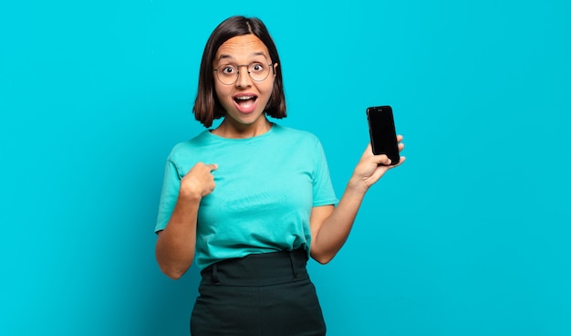 Young hispanic woman feeling happy, surprised and proud, pointing to self with an excited, amazed look