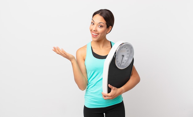 Young hispanic woman feeling happy, surprised realizing a solution or idea and holding a scale