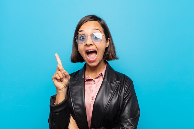 Young hispanic woman feeling like a happy and excited genius after realizing an idea cheerfully raising finger eureka