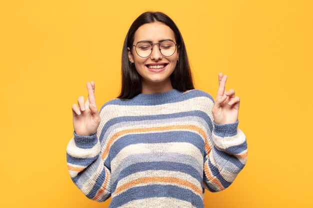 Young hispanic woman feeling nervous and hopeful, crossing fingers, praying and hoping for good luck