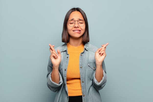 Young hispanic woman feeling nervous and hopeful, crossing fingers, praying and hoping for good luck