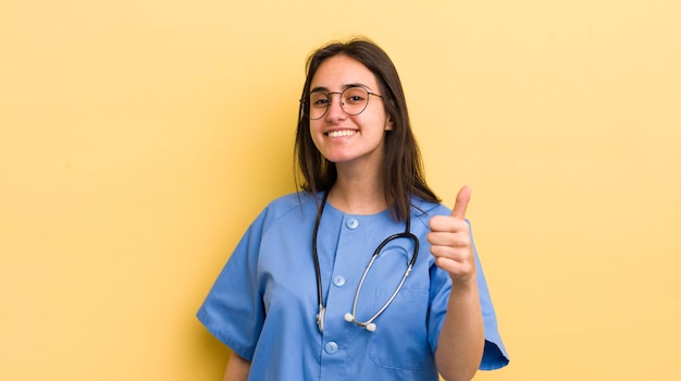 Young hispanic woman feeling proudsmiling positively with thumbs up nurse concept