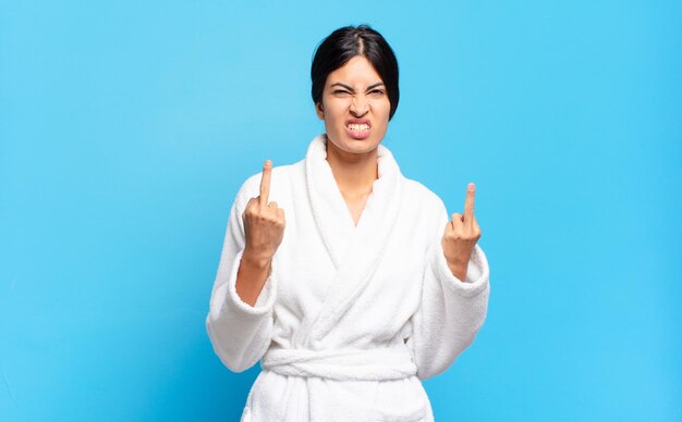 Young hispanic woman feeling provocative, aggressive and obscene, flipping the middle finger, with a rebellious attitude. bathrobe concept