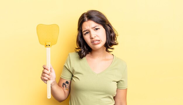 Young hispanic woman feeling puzzled and confused. kill flies concept