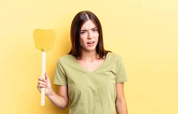 Young hispanic woman feeling puzzled and confused kill flies concept