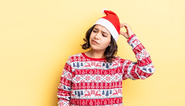 Young hispanic woman feeling puzzled and confused, scratching head. christmas concept