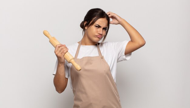 Young hispanic woman feeling puzzled and confused, scratching head and looking to the side