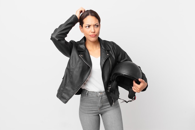 Young hispanic woman feeling puzzled and confused scratching head motorbike rider concept