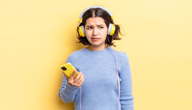 Foto giovane donna ispanica che si sente triste, sconvolta o arrabbiata e guarda di lato. cuffie e concetto di smartphone