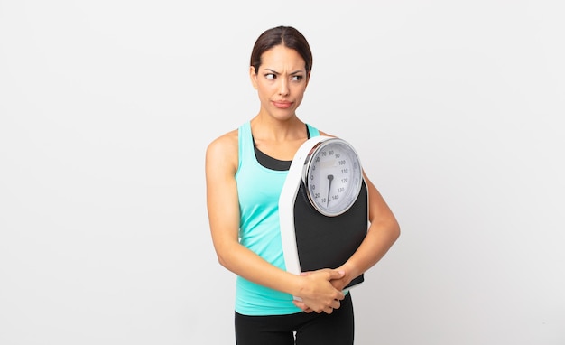 Young hispanic woman feeling sad, upset or angry and looking to the side and holding a scale