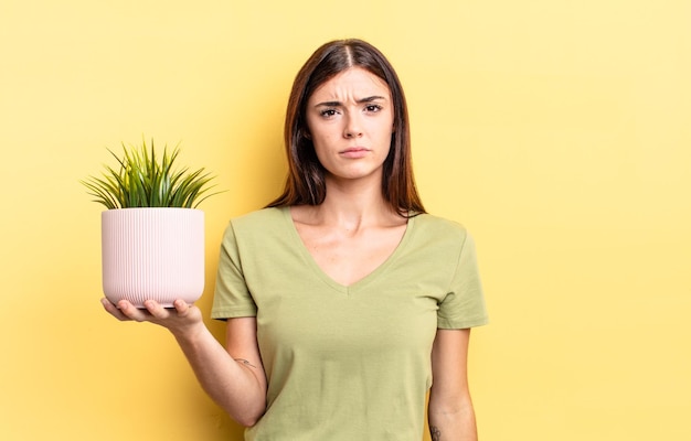 Young hispanic woman feeling sad and whiney with an unhappy look and crying. plant pot concept