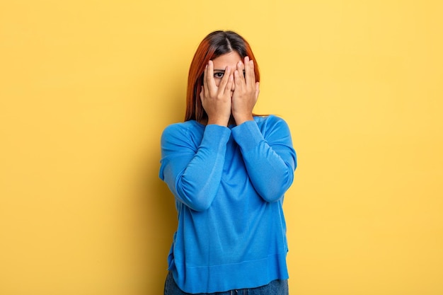 Young hispanic woman feeling scared or embarrassed peeking or spying with eyes halfcovered with hands