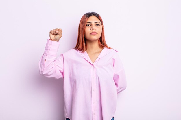 Young hispanic woman feeling serious, strong and rebellious, raising fist up, protesting or fighting for revolution