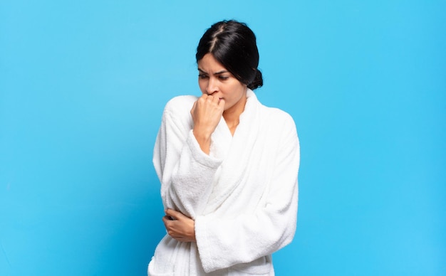 Young hispanic woman feeling serious, thoughtful and concerned, staring sideways with hand pressed against chin. bathrobe concept