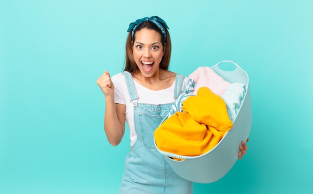 Young hispanic woman feeling shocked,laughing and celebrating success and washing clothes