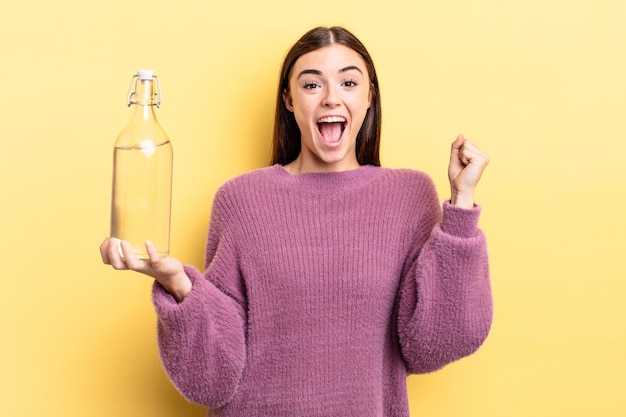 Young hispanic woman feeling shocked,laughing and celebrating success. water bottle concept