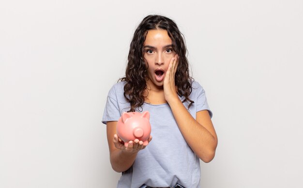 Young hispanic woman feeling shocked and scared, looking terrified with open mouth and hands on cheeks