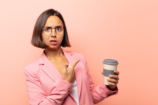 Young hispanic woman feeling shocked and surprised, pointing to copy space on the side with amazed, open-mouthed look