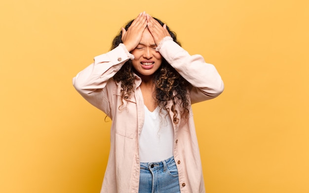 Young hispanic woman feeling stressed and anxious, depressed and frustrated with a headache, raising both hands to head