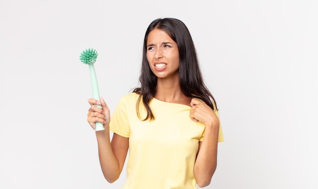 Young hispanic woman feeling stressed, anxious, tired and frustrated and holding a dish cleaning brush