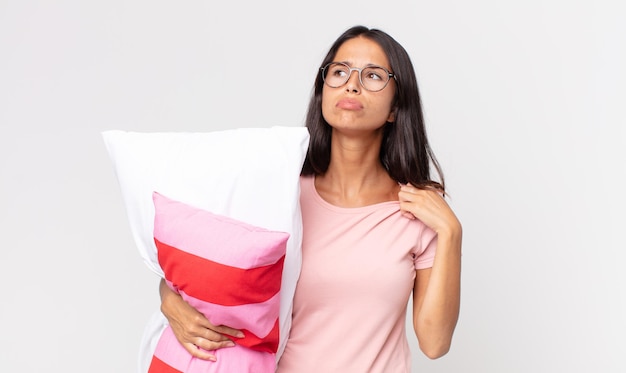 Young hispanic woman feeling stressed, anxious, tired and frustrated wearing pajamas and holding a pillow