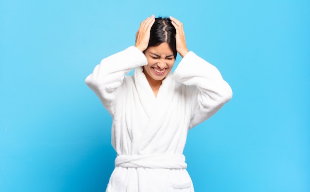 Young hispanic woman feeling stressed and frustrated, raising hands to head, feeling tired, unhappy and with migraine. bathrobe concept