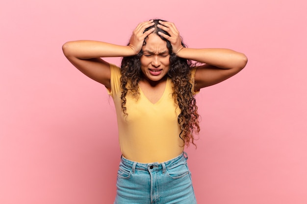 Young hispanic woman feeling stressed and frustrated, raising hands to head, feeling tired, unhappy and with migraine