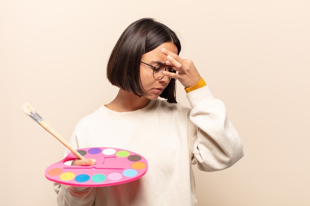 Young hispanic woman feeling stressed, unhappy and frustrated, touching forehead and suffering migraine of severe headache