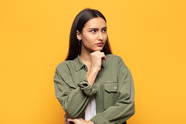 Young hispanic woman feeling thoughtful, wondering or imagining ideas, daydreaming and looking up to copy space