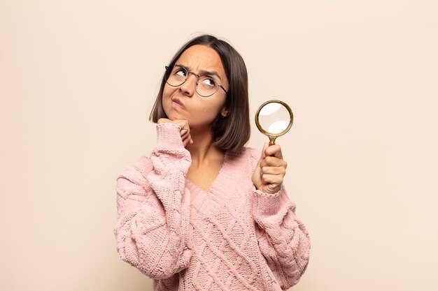 Young hispanic woman feeling thoughtful, wondering or imagining ideas, daydreaming and looking up to copy space