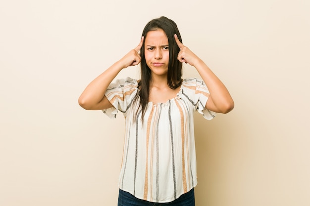 Young hispanic woman focused on a task, keeping forefingers pointing head.