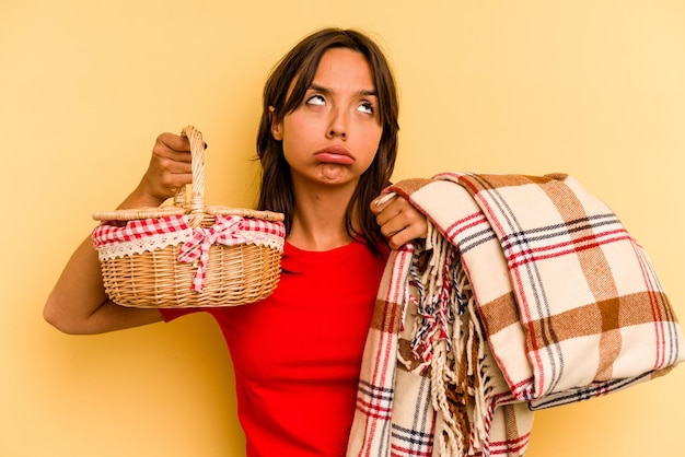 Young hispanic woman going to do it picnic isolated on yellow background