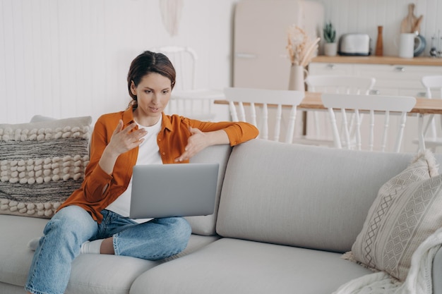 Young hispanic woman has online conference at home Lady is sitting on sofa having discussion