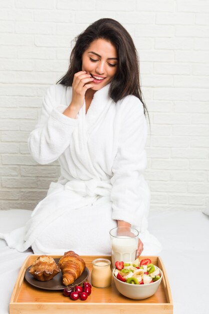 Young hispanic woman having breakfast on the bed