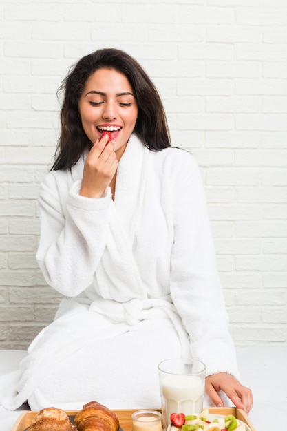 Young hispanic woman having breakfast on the bed