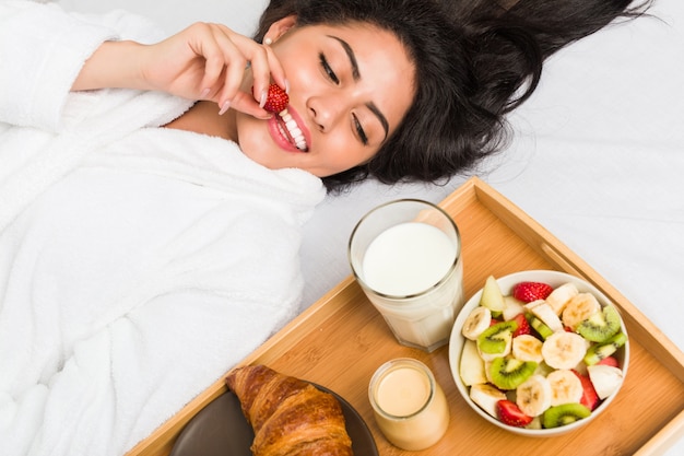 ベッドで朝食を持っている若いヒスパニック系女性