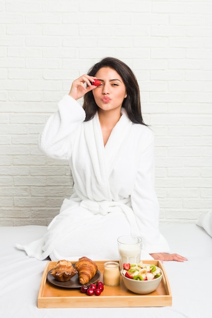 Young hispanic woman having breakfast on the bed