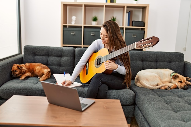 自宅で犬と一緒にソファに座ってオンラインギタークラスを持つ若いヒスパニック系女性