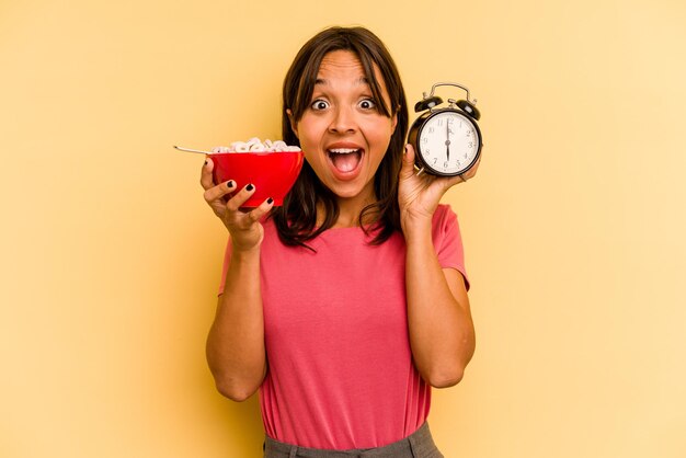 Young hispanic woman having a quick breakfast isolated on yellow background