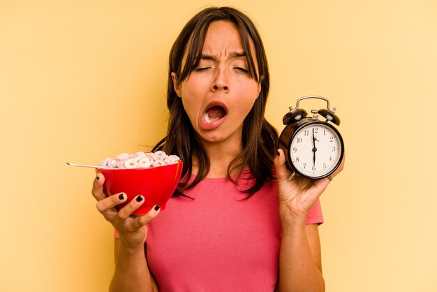 Young hispanic woman having a quick breakfast isolated on yellow background