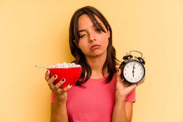 Young hispanic woman having a quick breakfast isolated on yellow background