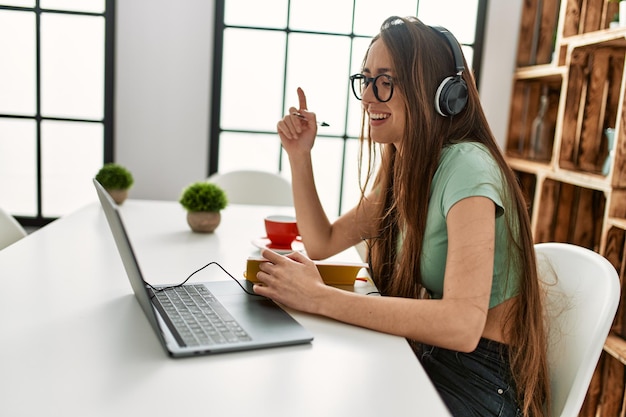 Young hispanic woman having video call sitting on table at home