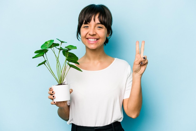 写真 指で2番目を示す青い背景で隔離の植物を保持している若いヒスパニック系の女性