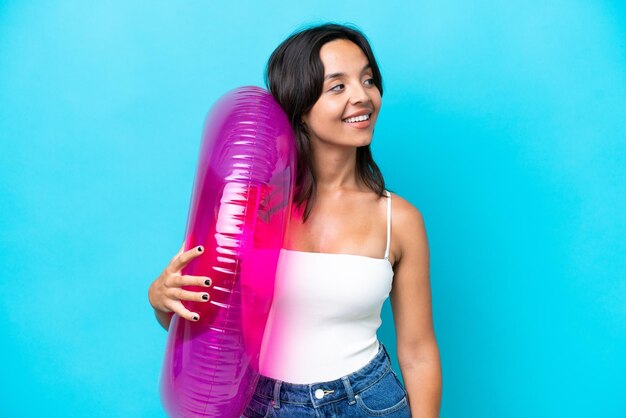 Young hispanic woman holding air mattress donut isolated on blue background looking side
