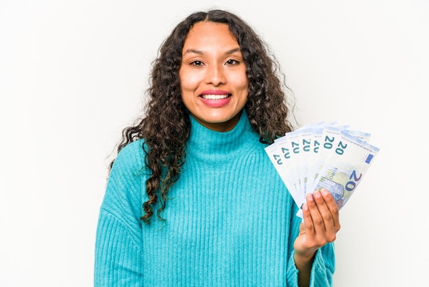 Young hispanic woman holding banknotes isolated on white background happy smiling and cheerful