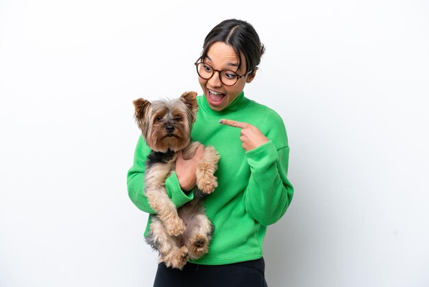 Young hispanic woman holding a dog isolated on white background\
with surprise facial expression