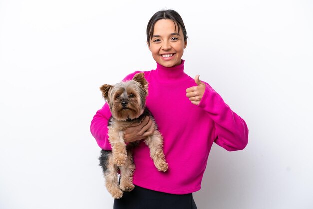 Photo young hispanic woman holding a dog isolated on white background with thumbs up because something good has happened