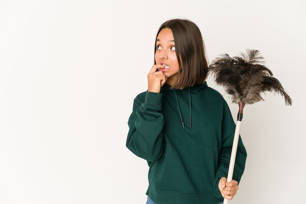 Young hispanic woman holding a duster relaxed thinking about something looking at a copy space.