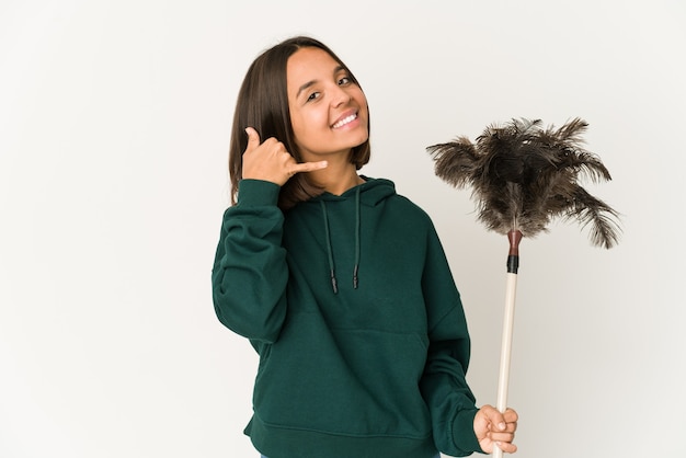 Young hispanic woman holding a duster showing a mobile phone call gesture with fingers